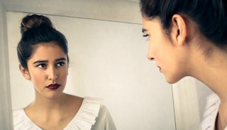 A young black-haired lady with an updo and dark red lipstick looking at herself in the mirror