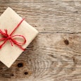 A gift wrapped in beige wrapping paper, with a red strap and bow, placed on a wooden floor during a ...