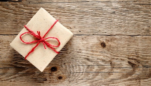 A gift wrapped in beige wrapping paper, with a red strap and bow, placed on a wooden floor during a ...