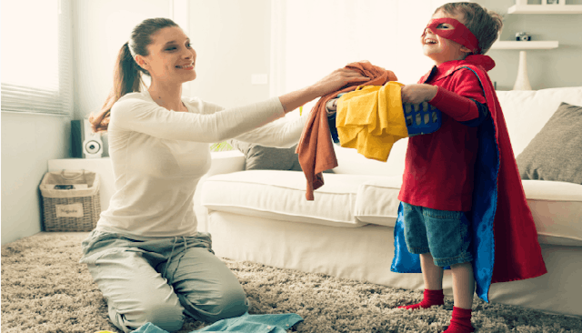 A mother giving washed laundry to her son, who is wearing a Superman costume