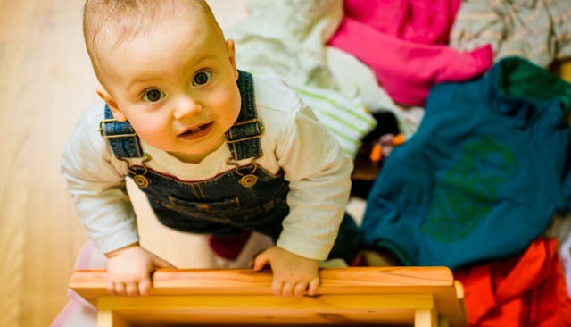 A baby boy looking up toward the camera while opening the drawer in a messy room.