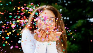 A woman blowing in her hands full of confetti, celebrating the small victories any mom can appreciat...