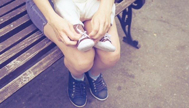 A mother sitting on a bench while holding her child on her lap and tying the child's shoe laces