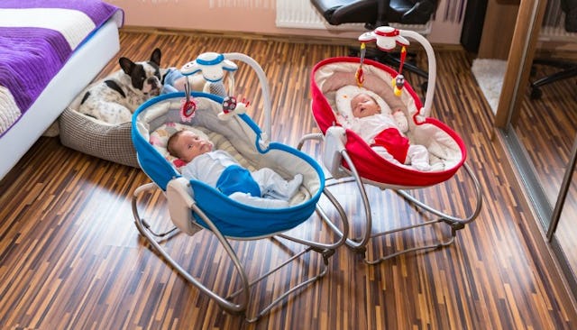 Twins in a red and a blue rocker napper baby seat in a bedroom