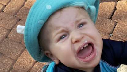 A child with a blue hat acting out in public, crying while looking at his parents