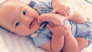 A baby with Down Syndrome holding its feet and smiling