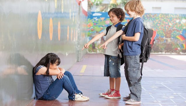 Two boys making fun of a little girl sitting on the ground