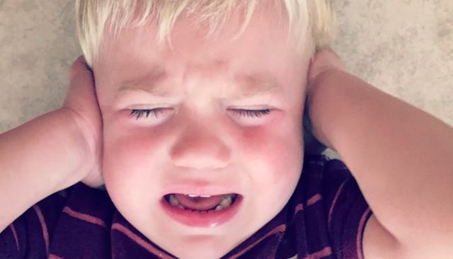 An autistic boy crying and covering his ears in a blue shirt with red stripes