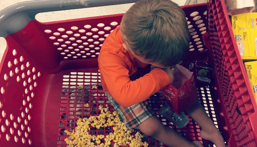 An autistic boy in a long-sleeved orange shirt and checked shorts sitting and eating popcorn in a re...