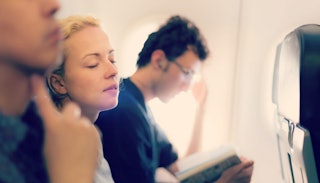 A blonde mom sitting in the middle plane seat between two men