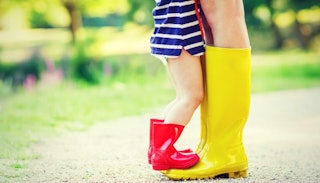 A three-year-old girl in red rain boots standing on mother's yellow rain boots 