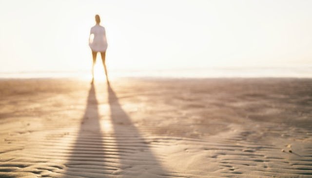 Blurred-out woman looking at a sunset, illuminated by the descending sun rays