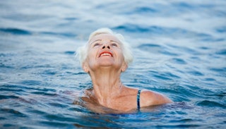 An elderly woman swimming in water above her neck and looking up toward the sky