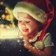 A child with a Santa cap opening a Christmas gift box with sparkles and glitter flying out of it