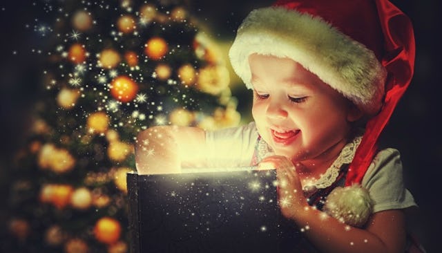 A child with a Santa hat opening a Christmas gift box with sparkles and glitter flying out of it