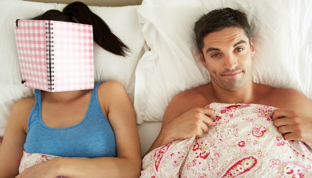 A man and woman lying in a bed, and the woman has a notebook over her face as a sign that they are n...