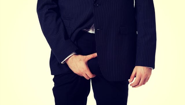 A man in blue suit with his hand holding his intimate parts