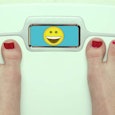A woman with a red pedicure measuring her weight with happy emoji in the measuring display