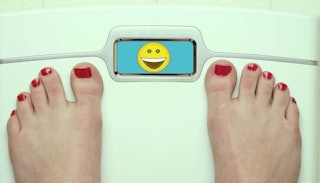 A woman with a red pedicure measuring her weight with a happy emoji in the measuring display
