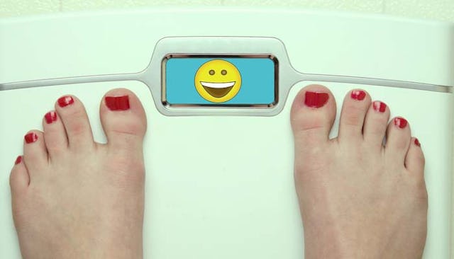 A woman with a red pedicure measuring her weight with a happy emoji in the measuring display