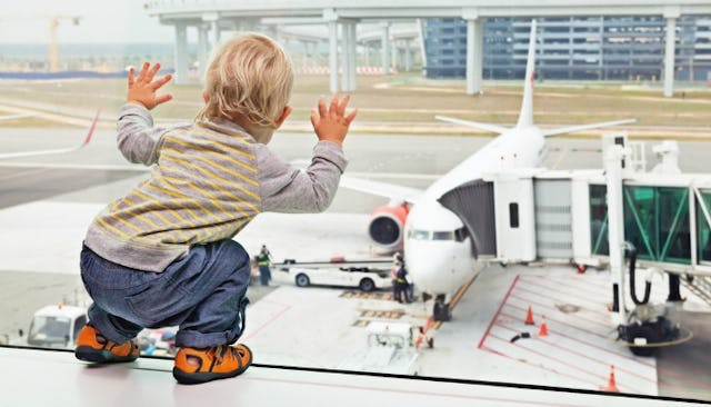 A little boy looking at a parked airplane while leaning against the airport glass windows