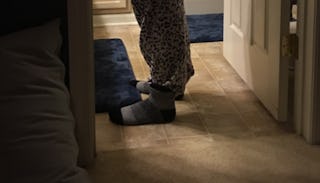 Close of feet in grey socks and grey sweatpants standing on beige bathroom tiles with small navy-blu...