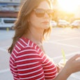 Brunette single mom in a parking field during sunset wearing a red shirt with thin white stripes and...