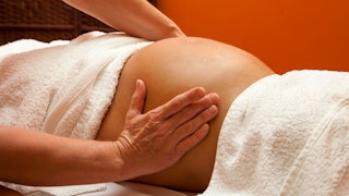 A pregnant woman lying while covered with white towel and only her belly exposed during a massage
