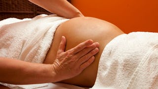 A pregnant woman lying while covered with white towel and only her belly exposed during a massage