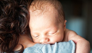 A newborn, resting its head and sleeping on a brown-haired woman's shoulder