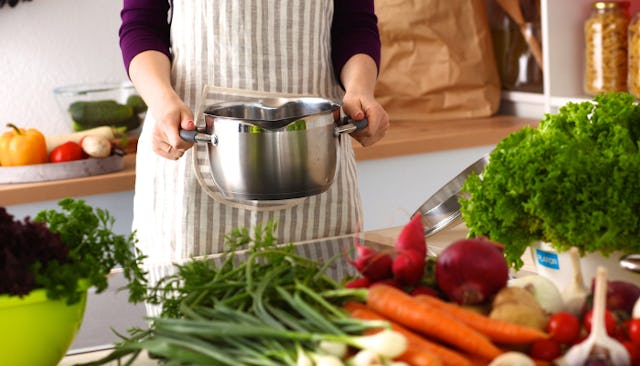 A woman holding a pot above the kitchen counter full of vegetables.