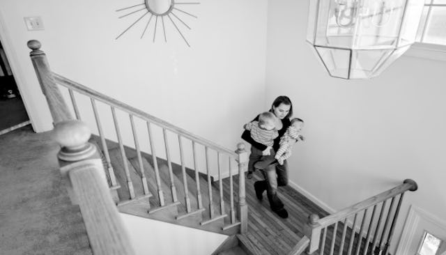A mother walking down a staircase while carrying her two toddlers in her arms in black and white