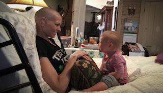 Joey Feek sitting in a bed with her baby opposite her, smiling at each other.