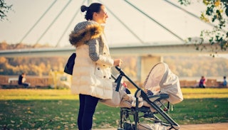 A young new mother standing next to her baby that is in a baby stroller