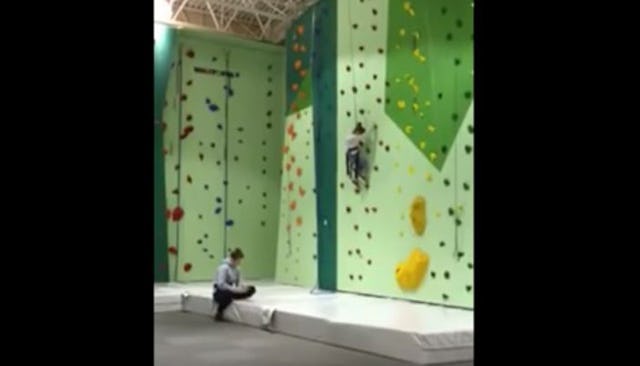 A crying girl stuck on a climbing wall and her instructor texting and not responding to her crying.
