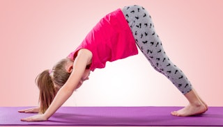 A girl in a pink shirt and grey trainers doing yoga at school