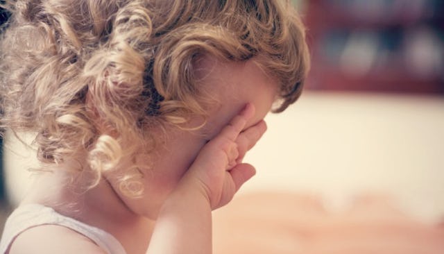 A blonde girl with curly hair holding her hands on her face like she is crying