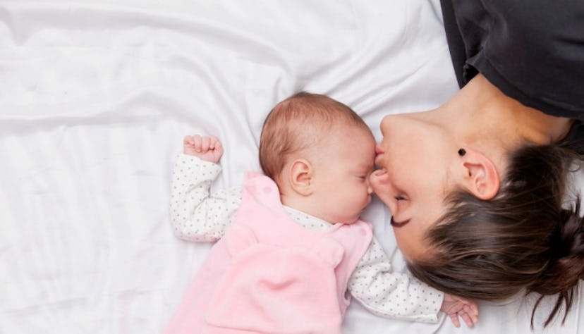 A mother kissing her newborn baby while the baby is sleeping