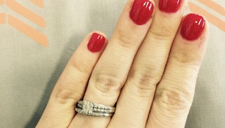 A close-up of a wedding ring on a woman's hand with red nail polish
