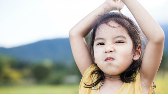 A strong-willed child with a smirk on her face, holding her hands over her head.