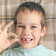 A boy holding his tooth and smiling, waiting for the tooth fairy 