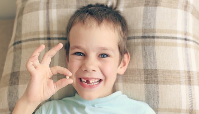 A boy holding his tooth and smiling, waiting for the tooth fairy