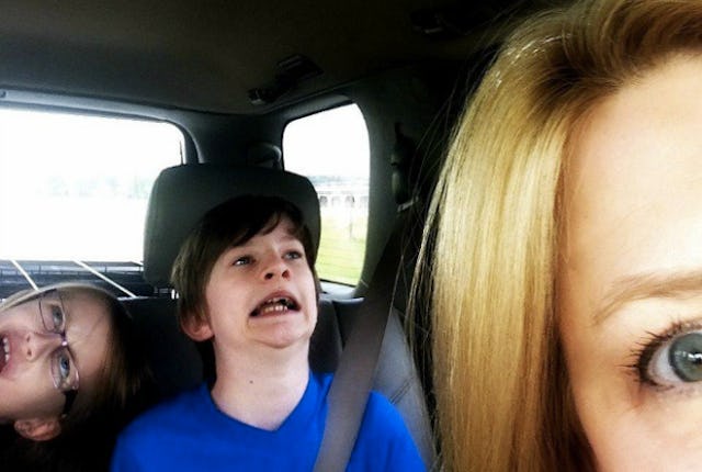A mother seated in a car, with her son and daughter playfully pulling funny facial expressions in th...