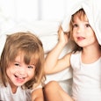 Two little girls peeking through white sheets in their shared bedroom