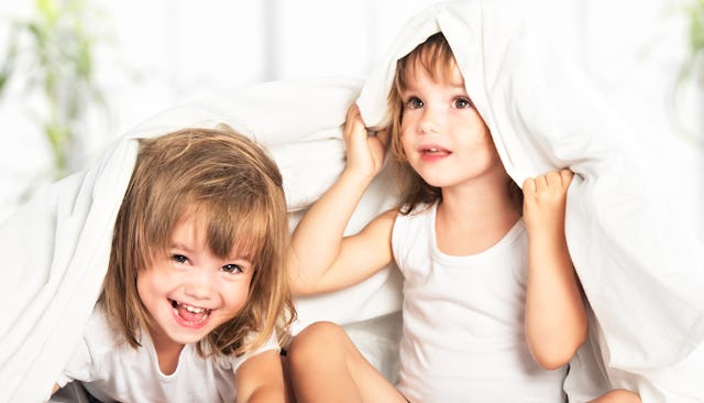 Two little girls peeking through white sheets in their shared bedroom