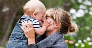 A nursery-school mom holding her toddler while she touches her face. 