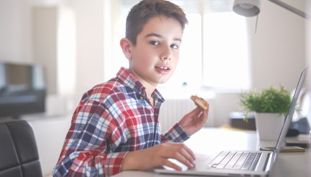 A boy at the laptop eating food after having talk with his mom