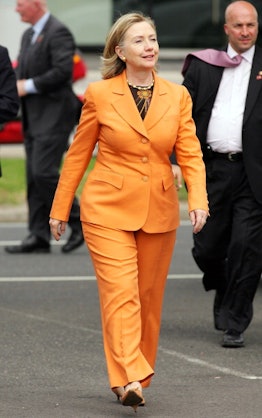 Hilary Clinton wearing an orange pantsuit, walking and smiling