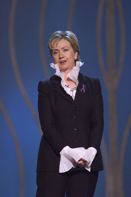  Hillary Clinton on stage wearing a black pantsuit and white shirt with a high collar 