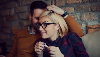 A couple sitting on a sofa, and the husband is being supportive and is kissing his wife's head